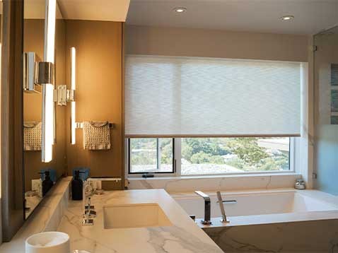 Upscale bathroom with a large window over the tub, covered by honeycomb shades